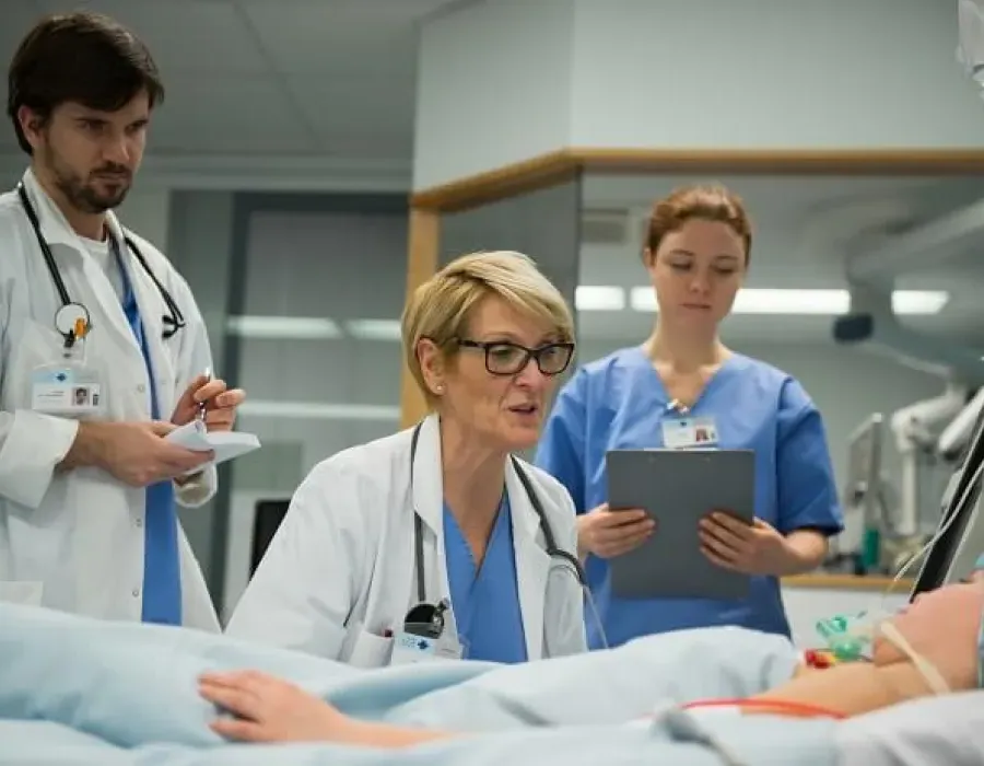 Family nurse practitioner seated at bedside with patient while nurses observe in hospital room